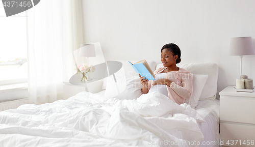 Image of happy pregnant african woman reading book at home