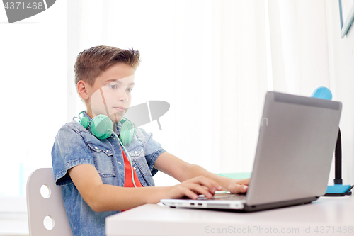 Image of happy boy with headphones typing on laptop at home