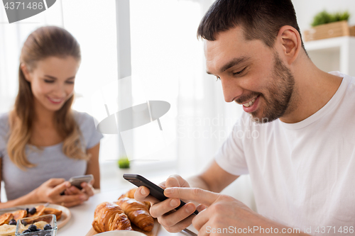 Image of couple with smartphones having breakfast at home