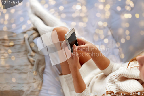 Image of happy young woman with smartphone in bed at home