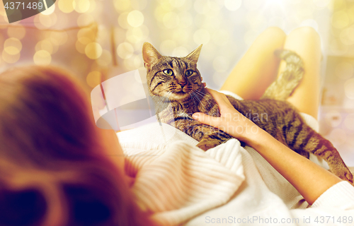 Image of happy young woman with cat lying in bed at home