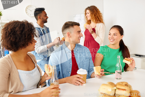 Image of happy friends or team eating at office