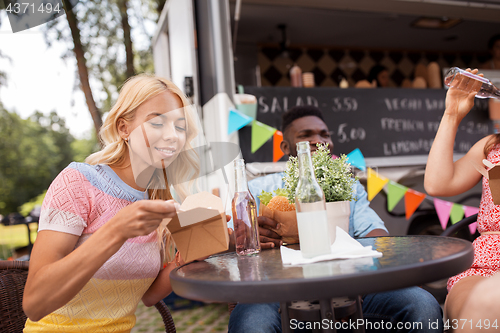 Image of happy friends with drinks eating at food truck