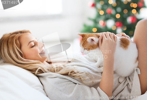 Image of happy young woman with cat in bed at christmas
