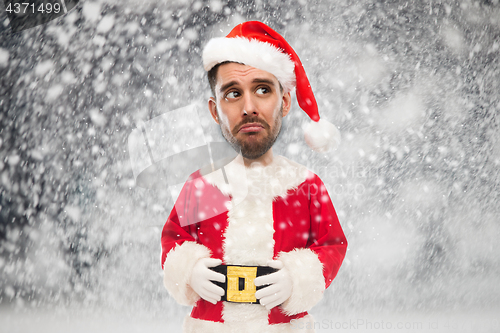 Image of sad man in santa claus costume over christmas snow