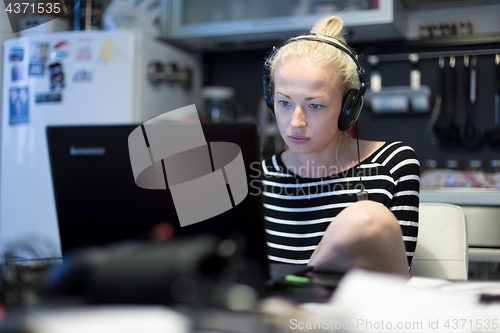 Image of Adult woman in her casual home clothing working and studying remotely from her small flat late at night.