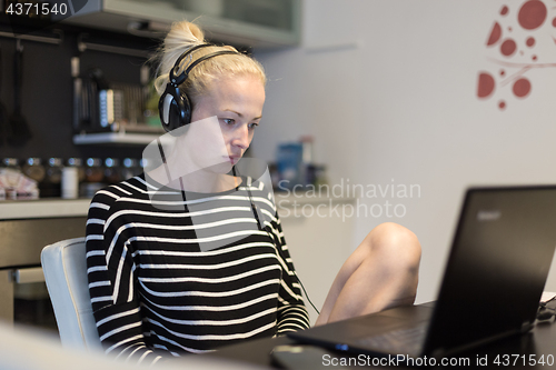 Image of Adult woman in her casual home clothing working and studying remotely from her small flat late at night.