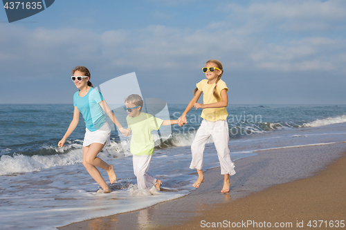 Image of Three happy children running on the beach at the day time.