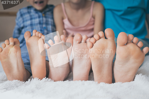 Image of Happy brother and sisters  sitting on the bed barefoot