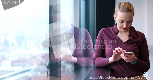 Image of Elegant Woman Using Mobile Phone by window in office building