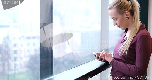 Image of Elegant Woman Using Mobile Phone by window in office building