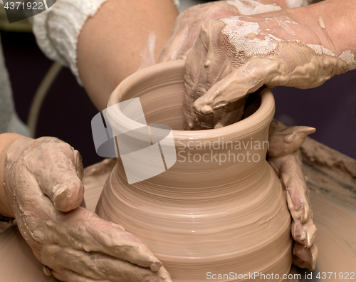 Image of Two women in process of making clay vase on pottery wheel