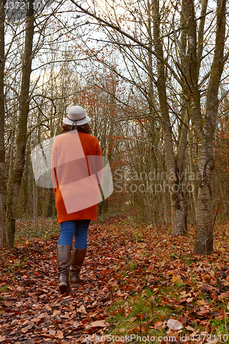 Image of Woman in warm cardigan and hat walking through autumnal woodland