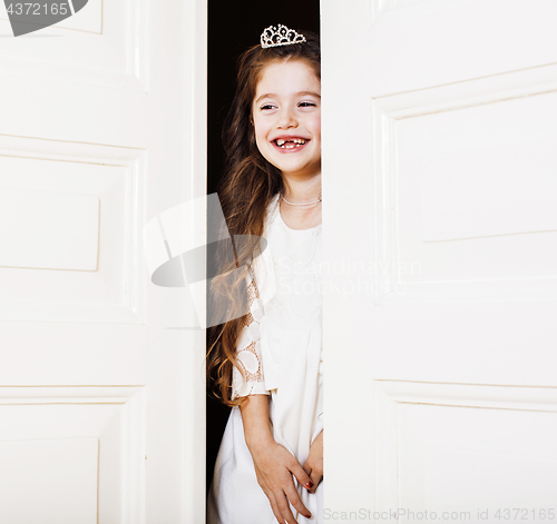 Image of little cute girl at home, opening door well-dressed in white dress, adorable milk fairy teeth, curious child 