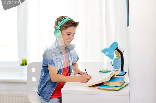 Image of student boy in headphones writing to notebook