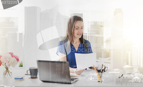 Image of happy woman with papers and laptop at office