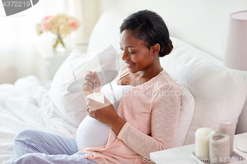 Image of pregnant woman eating yogurt in bed