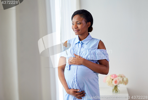 Image of pregnant woman looking through window at home