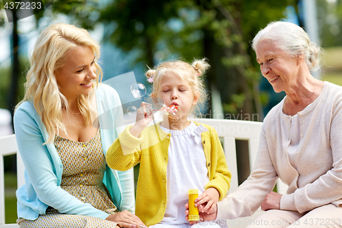 Image of happy family blowing soap bubbles at park