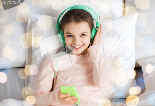 Image of girl with headphones listening to music in bed