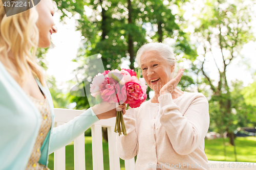 Image of daughter giving flowers to senior mother at park