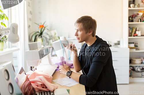 Image of fashion designer with smartphone working at studio