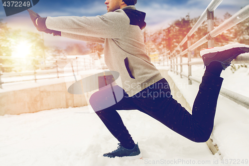 Image of sports man stretching leg at fence in winter