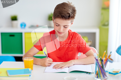 Image of happy student boy writing to notebook at home