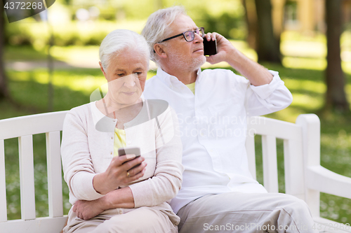 Image of happy senior couple with smartphones at park