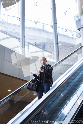 Image of Businesswoman with large black bag and mobile phone descending on escalator.