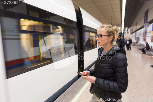 Image of Woman with a cell phone waiting for metro.