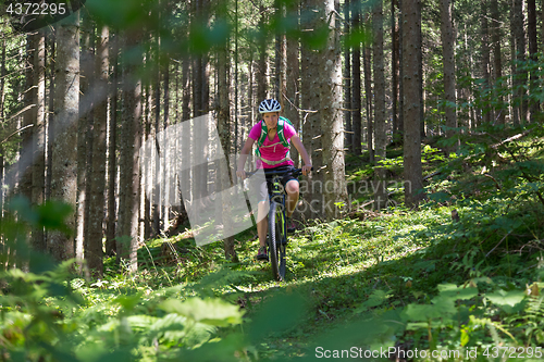 Image of Active sporty woman riding mountain bike on forest trail .