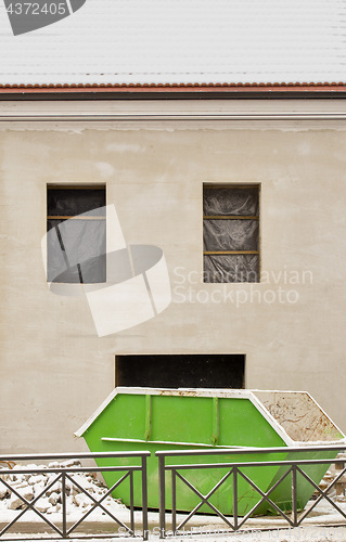 Image of Construction site. Big green trash container near the wall