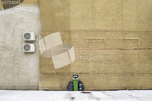 Image of Green recycle bin near the large brick wall