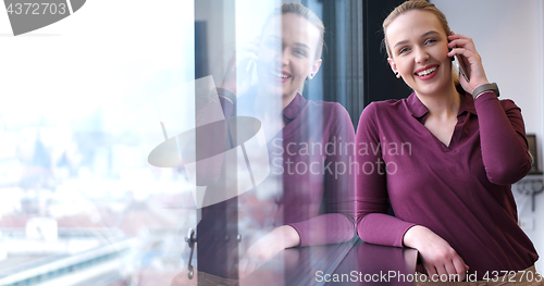 Image of Elegant Woman Using Mobile Phone by window in office building