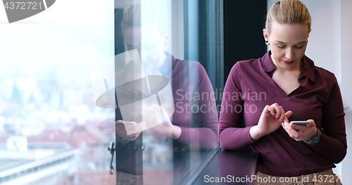 Image of Elegant Woman Using Mobile Phone by window in office building