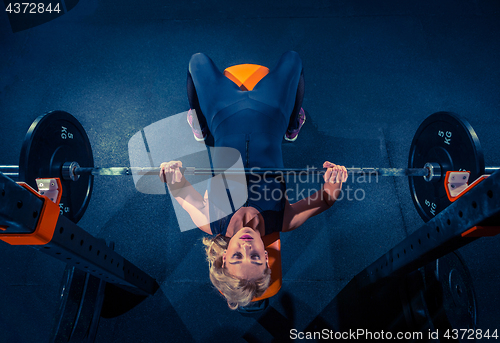 Image of Fit young woman lifting barbells looking focused, working out in a gym