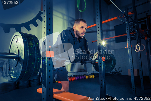 Image of Portrait of super fit muscular young man working out in gym with barbell