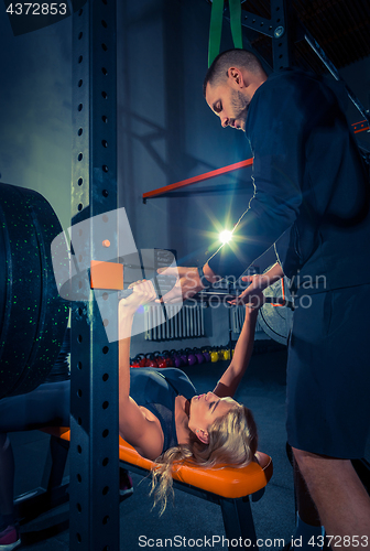Image of Fit young woman lifting barbells looking focused, working out in a gym
