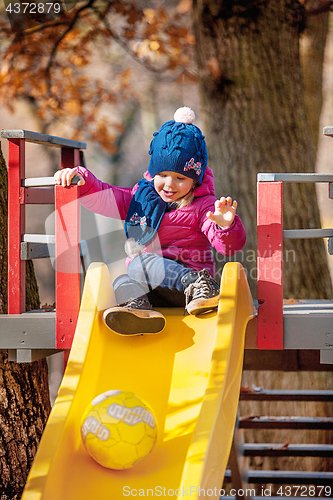 Image of Happy three-year baby girl in jacket on slide