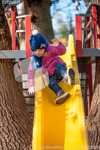 Image of Happy three-year baby girl in jacket on slide