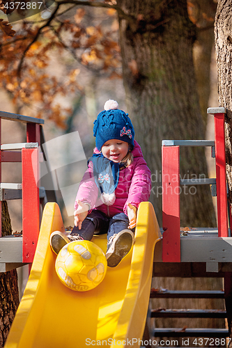 Image of Happy three-year baby girl in jacket on slide