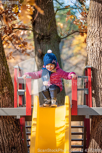 Image of Happy three-year baby girl in jacket on slide