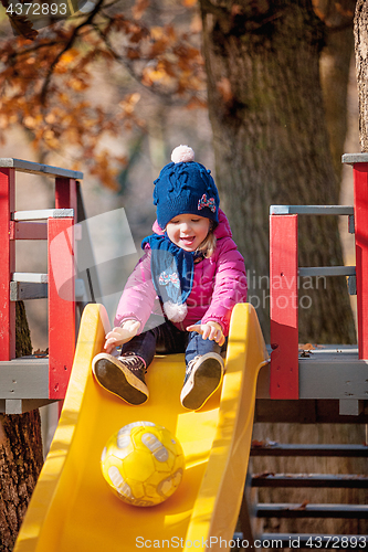 Image of Happy three-year baby girl in jacket on slide