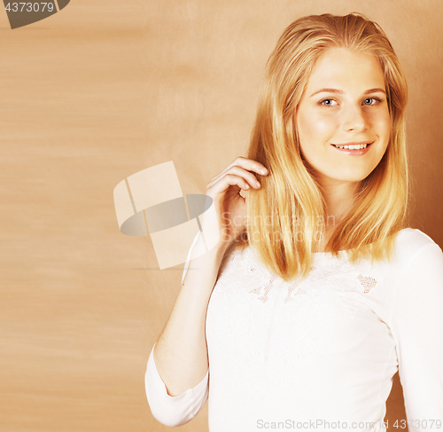 Image of young cool blong teenage girl messed with her hair smiling close up on warm brown background, lifestyle real people concept