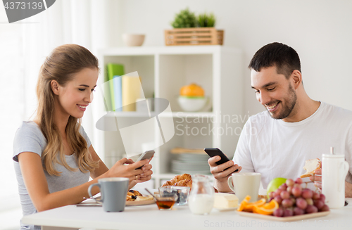 Image of couple with smartphones having breakfast at home