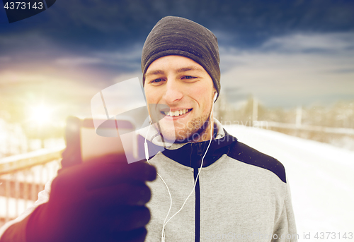 Image of happy man with earphones and smartphone in winter