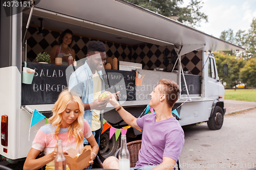 Image of happy friends with drinks eating at food truck