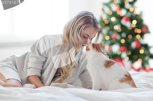 Image of happy young woman with cat in bed at christmas