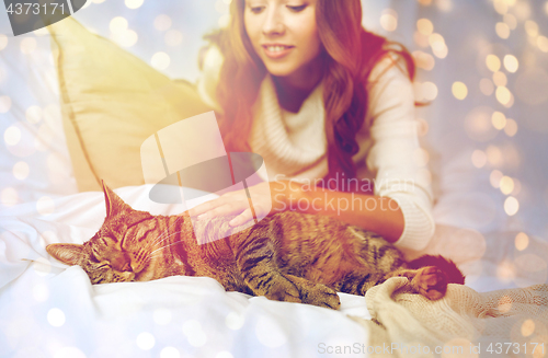 Image of happy young woman with cat lying in bed at home